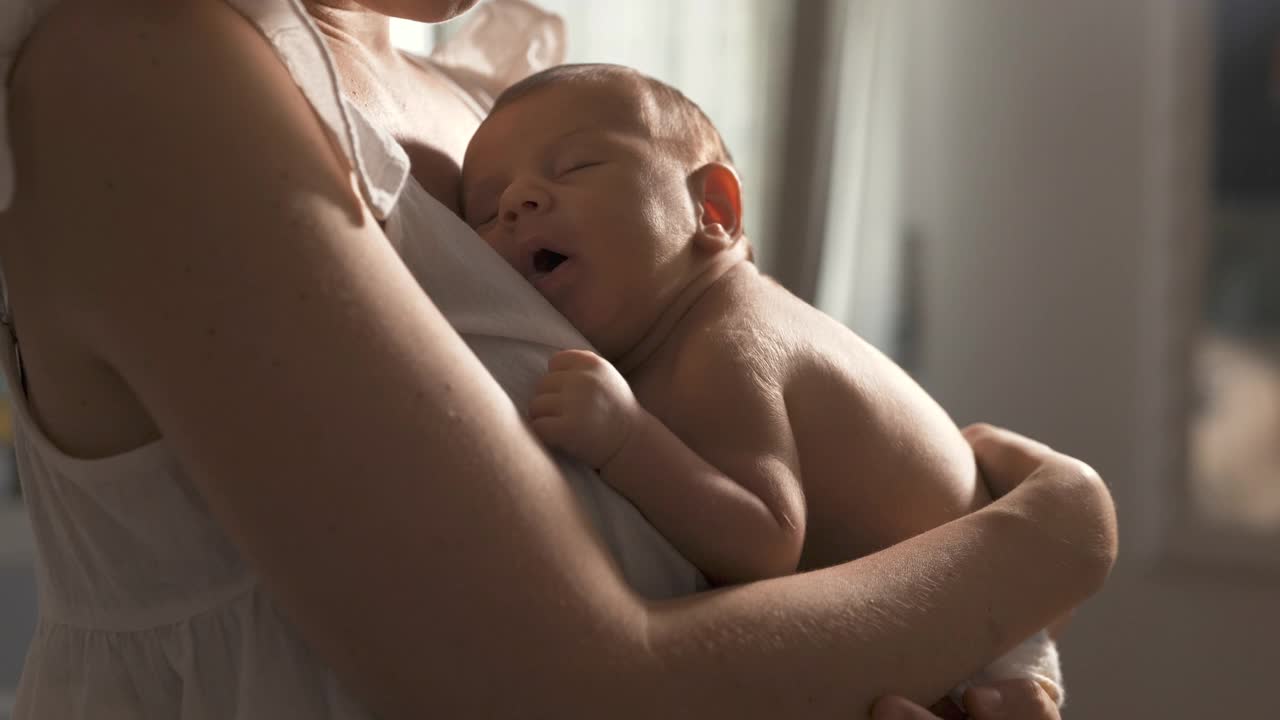 真实的新生婴儿在母亲的怀里安静地睡觉，她唱着摇篮曲给他听。小婴儿在父母的摇晃下做着快乐的梦。慢动作视频素材