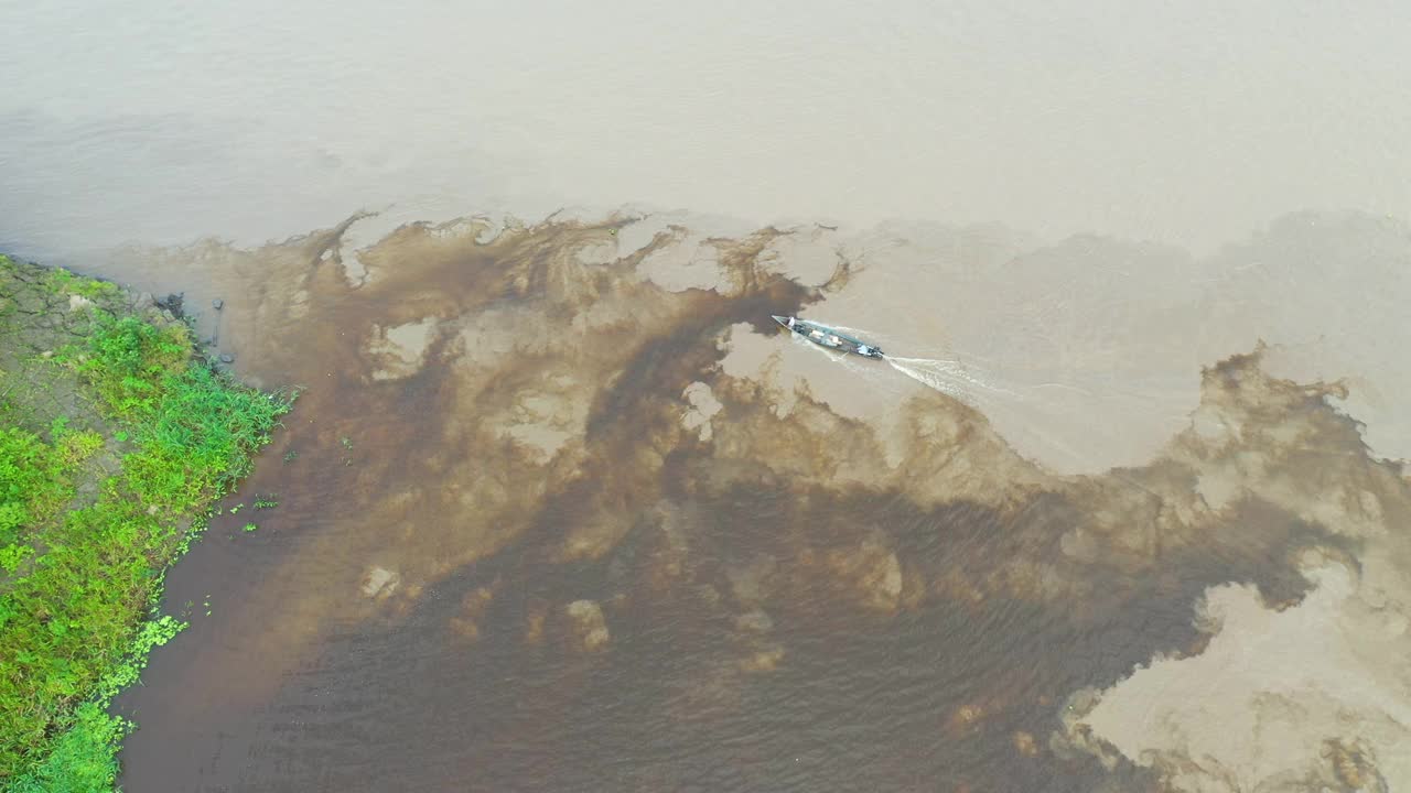 无人机跟踪一艘沿着秘鲁亚马逊河岸边行驶的小船视频素材