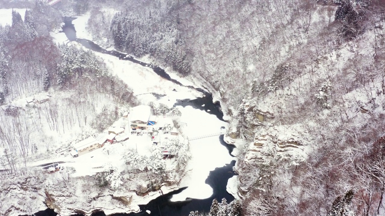 4K鸟瞰小村庄和河流之间的山被雪覆盖。视频素材