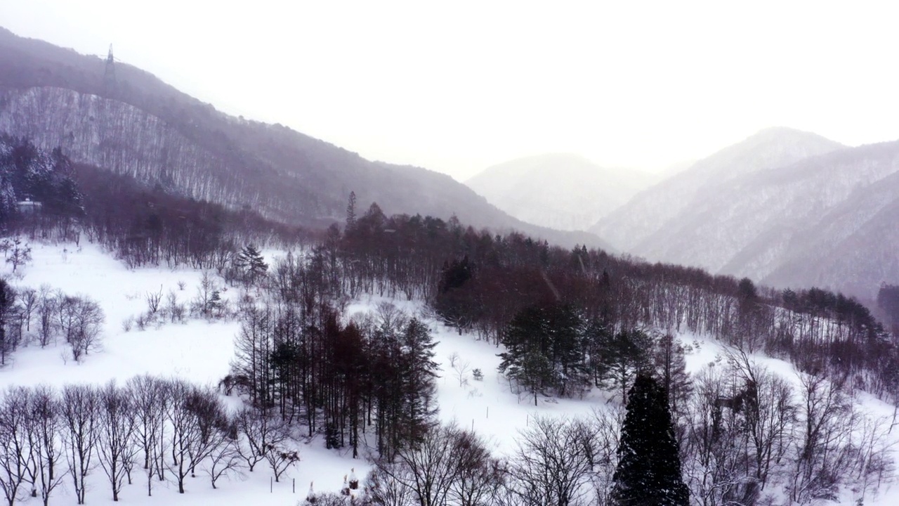 4K鸟瞰小村庄和河流之间的山被雪覆盖。视频素材