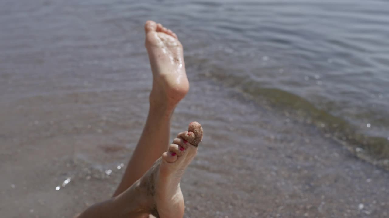 赤脚女孩躺在海边的海浪日光浴夏天周末近。女人微笑视频素材