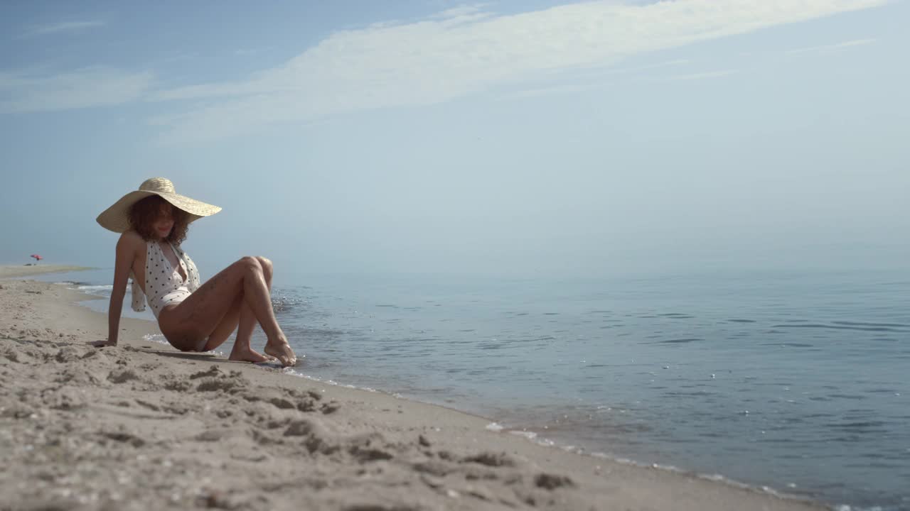 悠闲的女子坐在沙滩上，在海浪中洗腿。女孩日光浴。视频素材