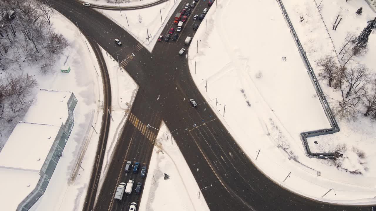 俯瞰一个冬季城市十字路口的汽车，雪躺着。视频下载