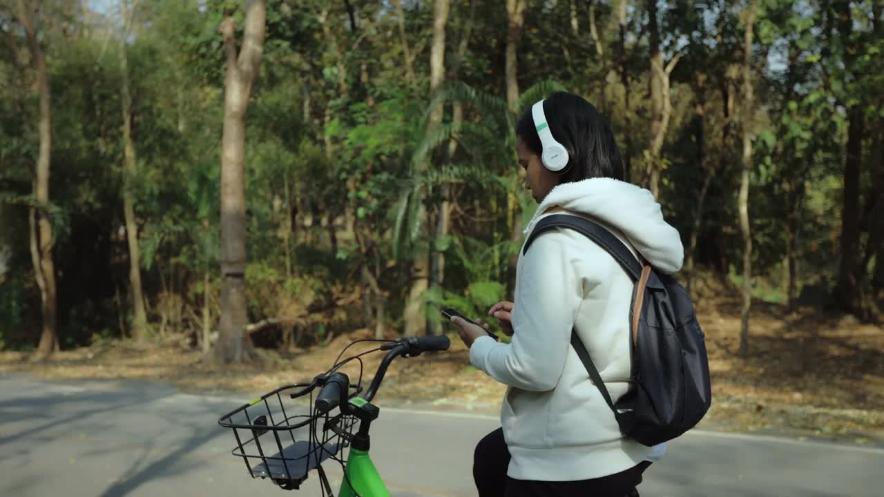 亚洲女子在公园里骑自行车，用智能手机看地图。女游客租了一辆自行车在城市里旅游。城市新型共享商业项目，生态交通。视频素材