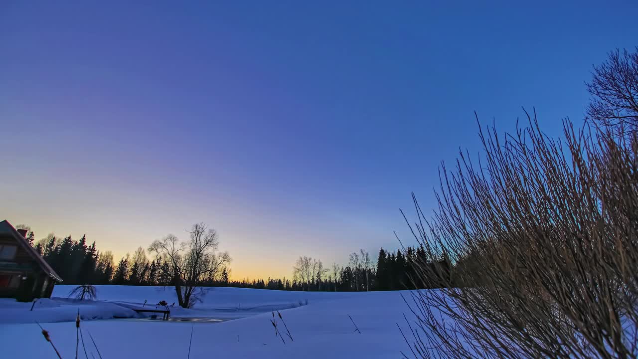 在寒冷的冬天，雪地里，美丽的日出在木屋上空，时间流逝的镜头。视频素材