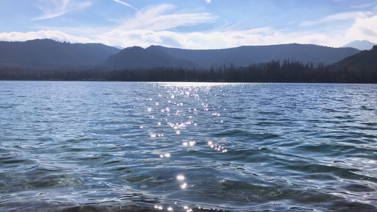 阳光反射在森林和山脉附近的湖面上，闪闪发光视频素材