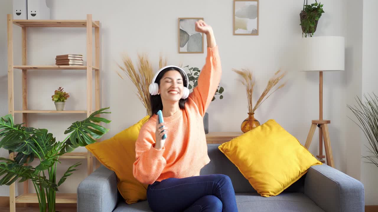 快乐的女人戴着耳机使用智能手机和跳舞听音乐视频素材