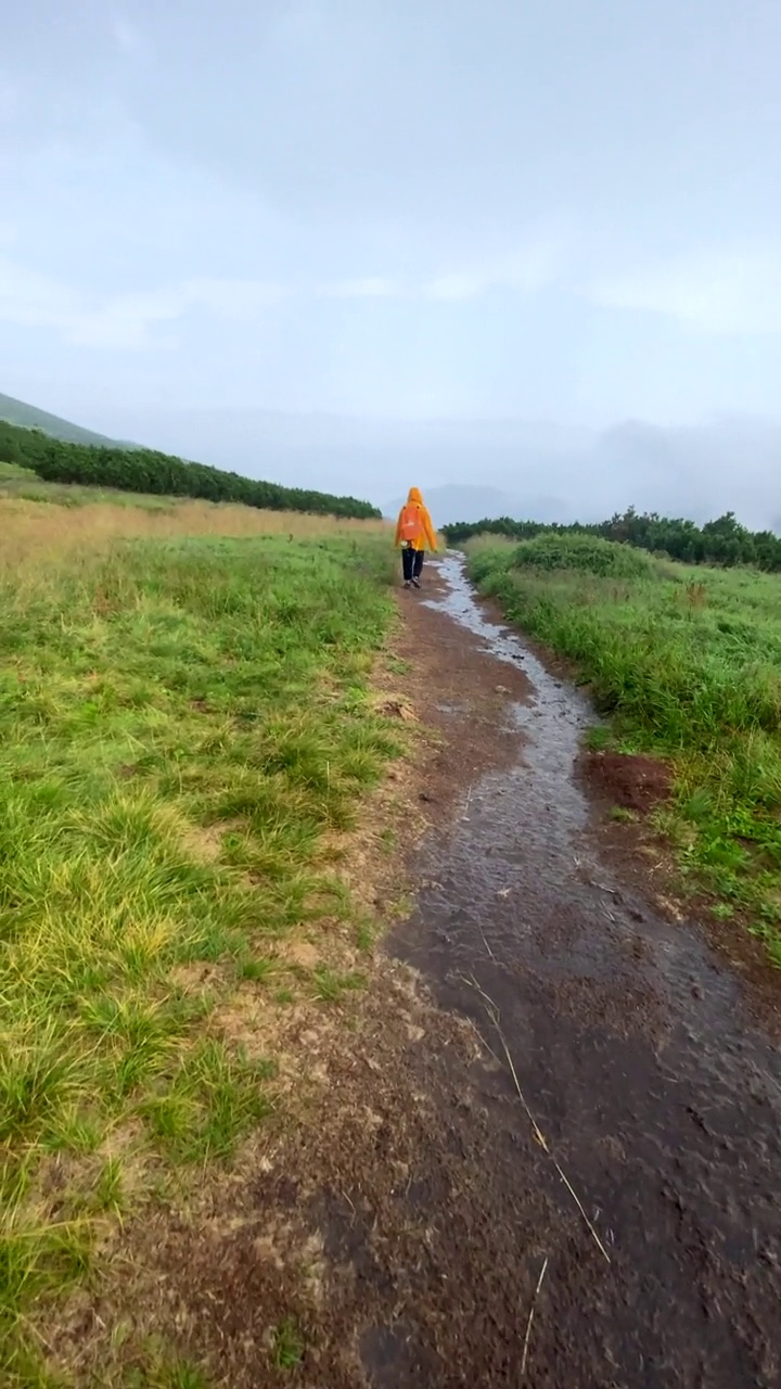 第一人称观走在湿山尾巴女人在黄色雨衣前面视频素材