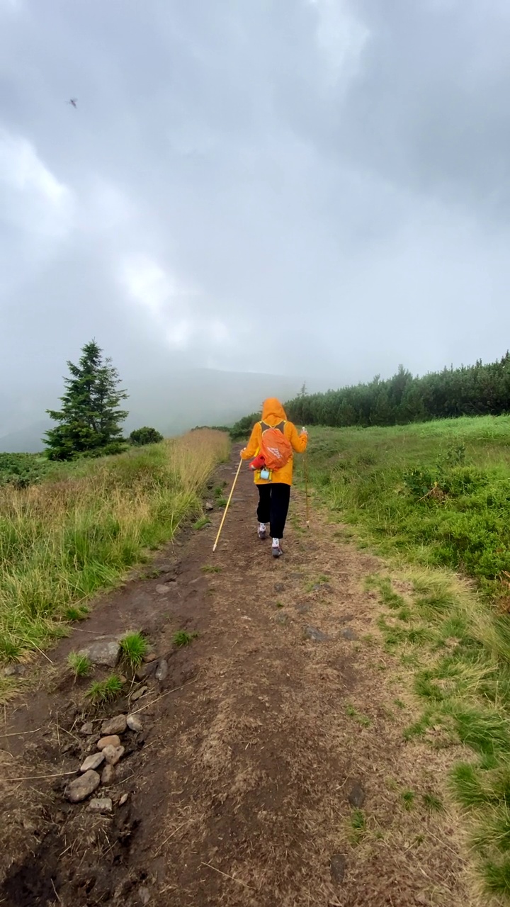 在下雨的天气里，穿着黄色雨衣的女人沿着岩石小径走视频素材