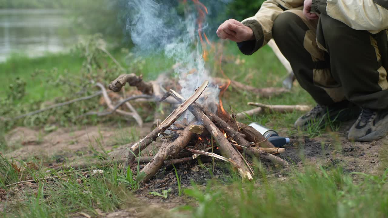 特写剪裁的不认识的冻结渔民在河边的火上温暖的手，在日落前做饭。视频素材