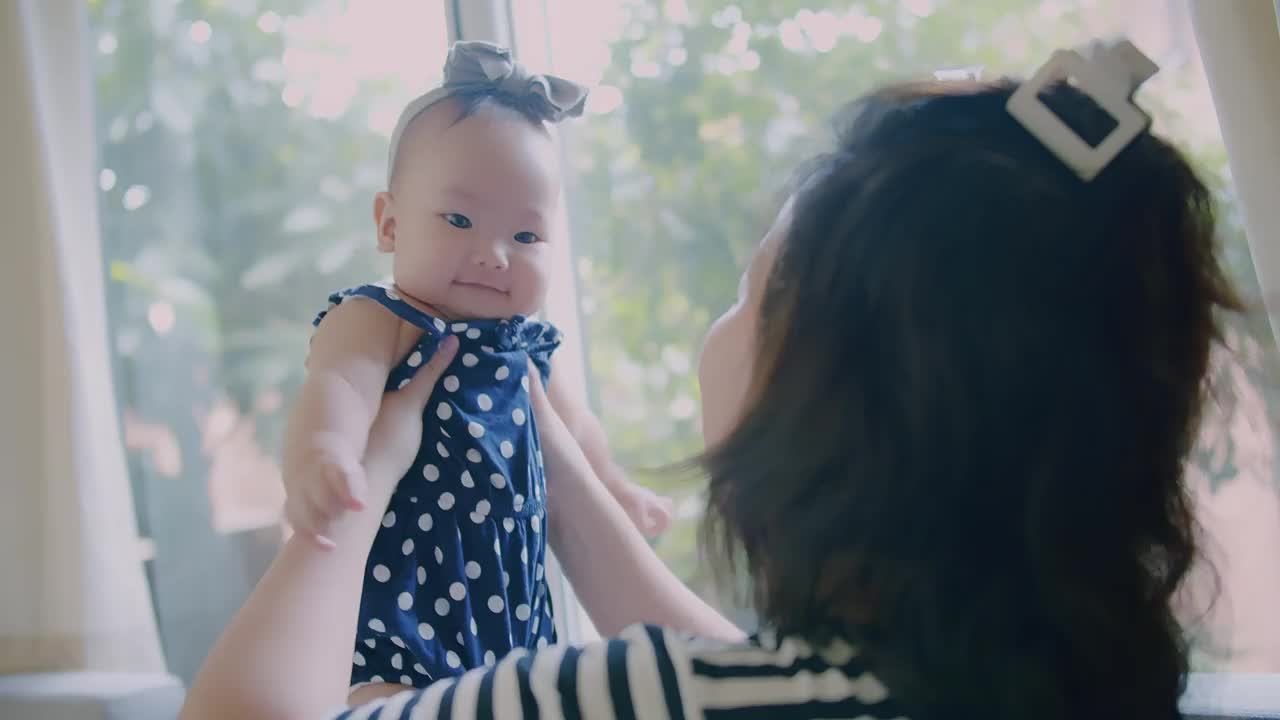 快乐的亚洲家庭母亲年轻的女人抱着可爱可爱的婴儿婴儿一起玩，在家里带着有趣的微笑笑脸，母爱关怀童年的生活时刻视频素材