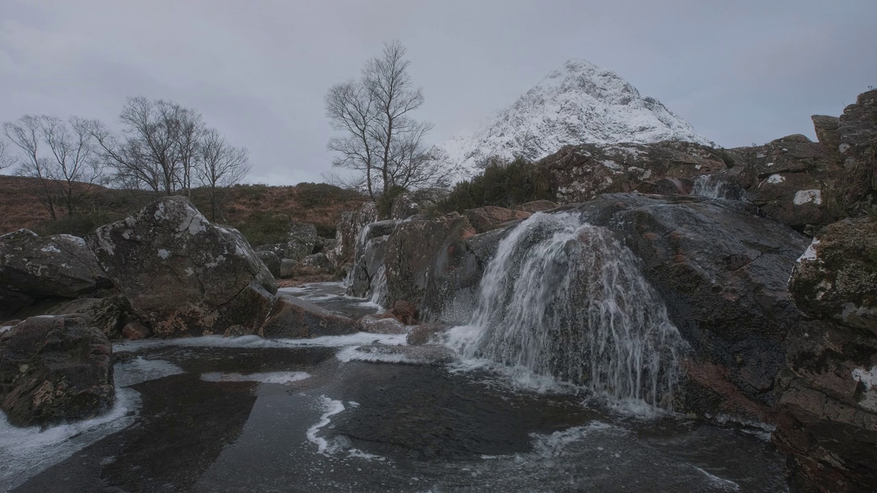 在白雪覆盖的Buachaille Etive Mor脚下，山间河流和部分冻结的瀑布的4k镜头视频下载