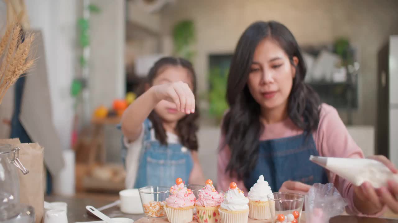 母女俩在纸杯蛋糕上撒配料。视频素材