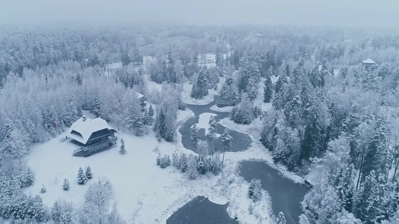 在冬天，无人机拍摄了冰湖旁的针叶林和小木屋的积雪覆盖的树木。视频素材