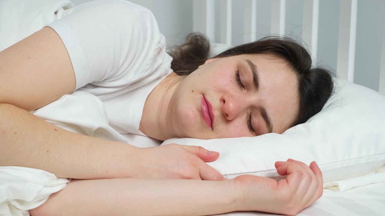 一个年轻的褐发女人打着哈欠，躺在床上的枕头上。视频素材