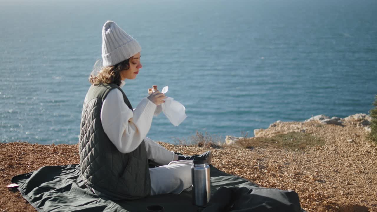 女孩独自在悬崖边吃海洋野餐。宁静的游客欣赏风景视频素材