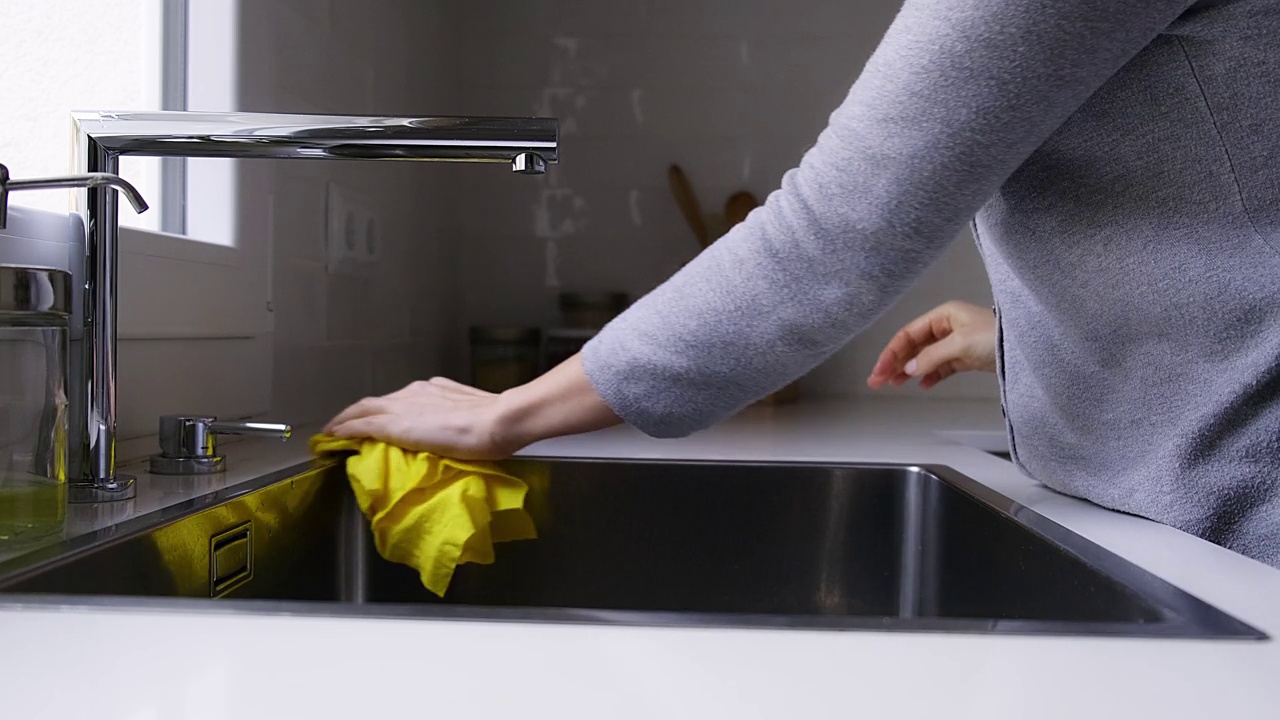 4k视频中，一名无法辨认的女子用湿黄色清洁布擦拭水槽和水龙头。挤压布。家务和卫生视频素材