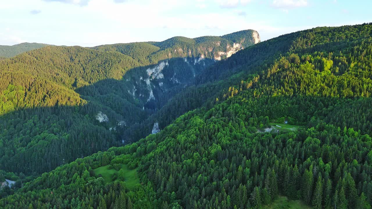 一条路经过布满云杉森林和草地的山丘，映衬着多云的天空视频素材