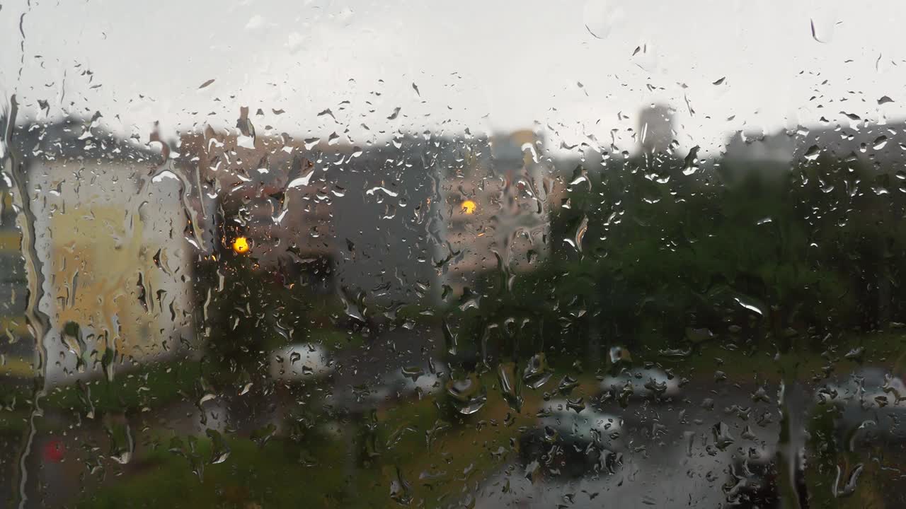 雨天玻璃窗上的雨滴。水从上面滴下来。模糊的背景。这个城市的天气很糟糕。建筑，房子，窗外的汽车。气象学和天气预报。暗晦视频素材