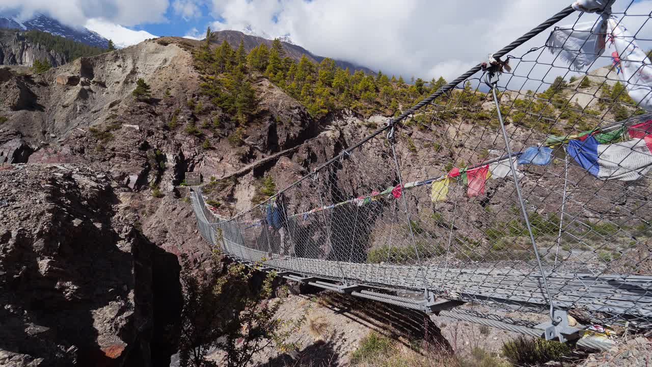 一个年轻人在尼泊尔卡利甘达基峡谷徒步旅行时穿过一座吊桥。视频素材