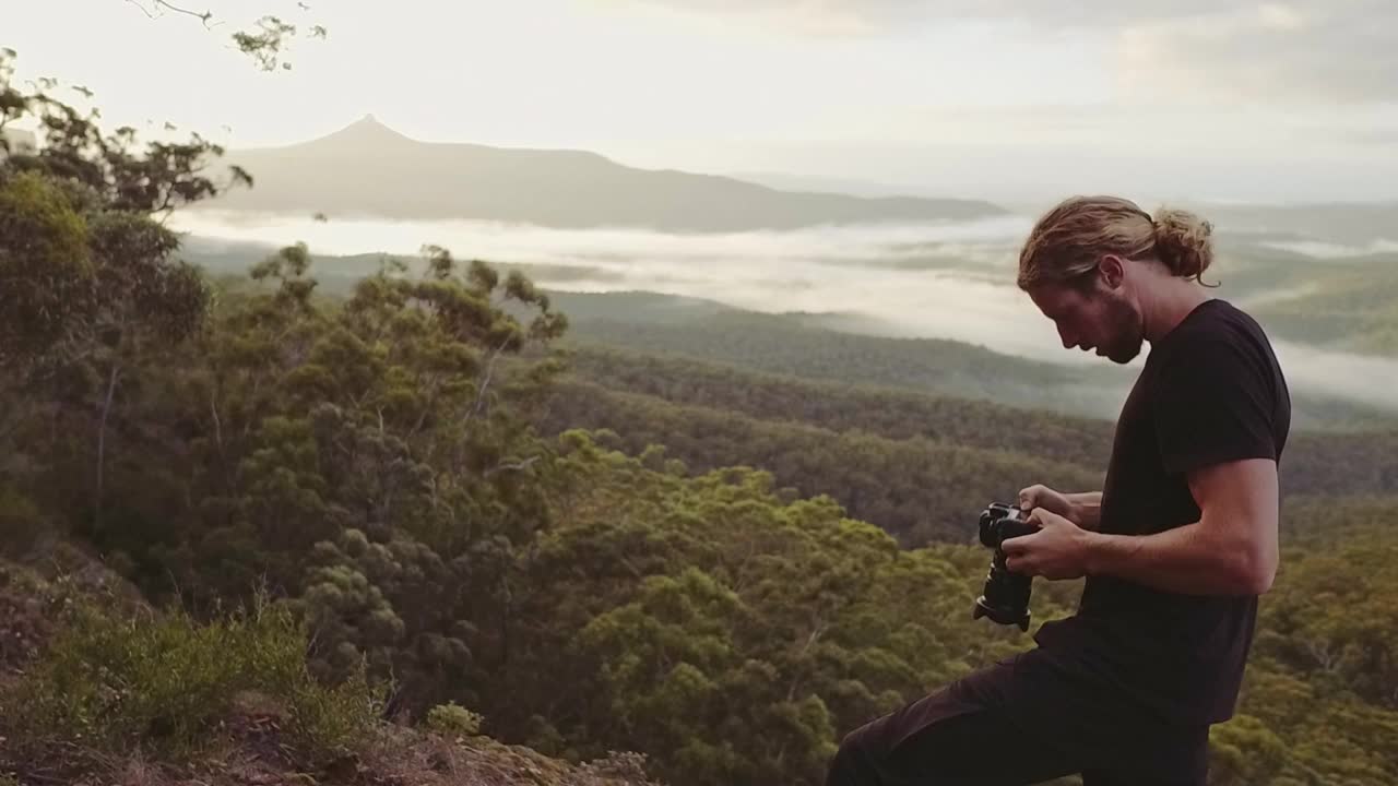 年轻男子背包旅行时在山边拍摄日出的照片视频素材