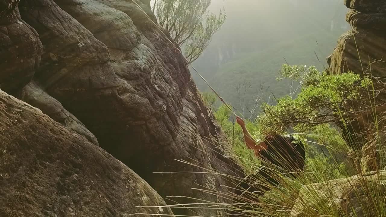 年轻人背着背包，用绳子爬上了山的边缘视频素材