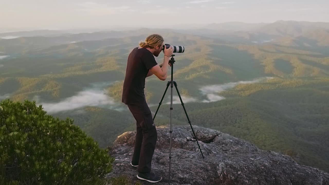 年轻男子背包旅行时在山边拍摄日出的照片视频素材