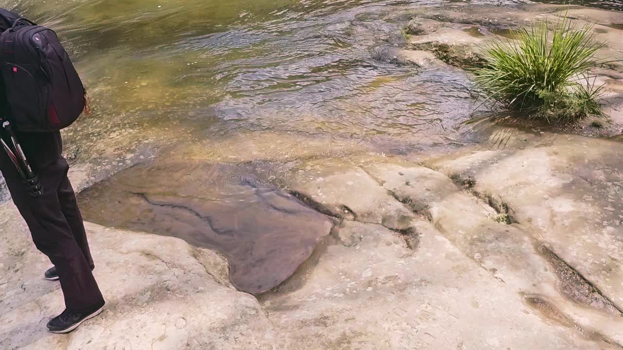 一个年轻人正在拍摄山上的瀑布和湍急的溪流视频素材