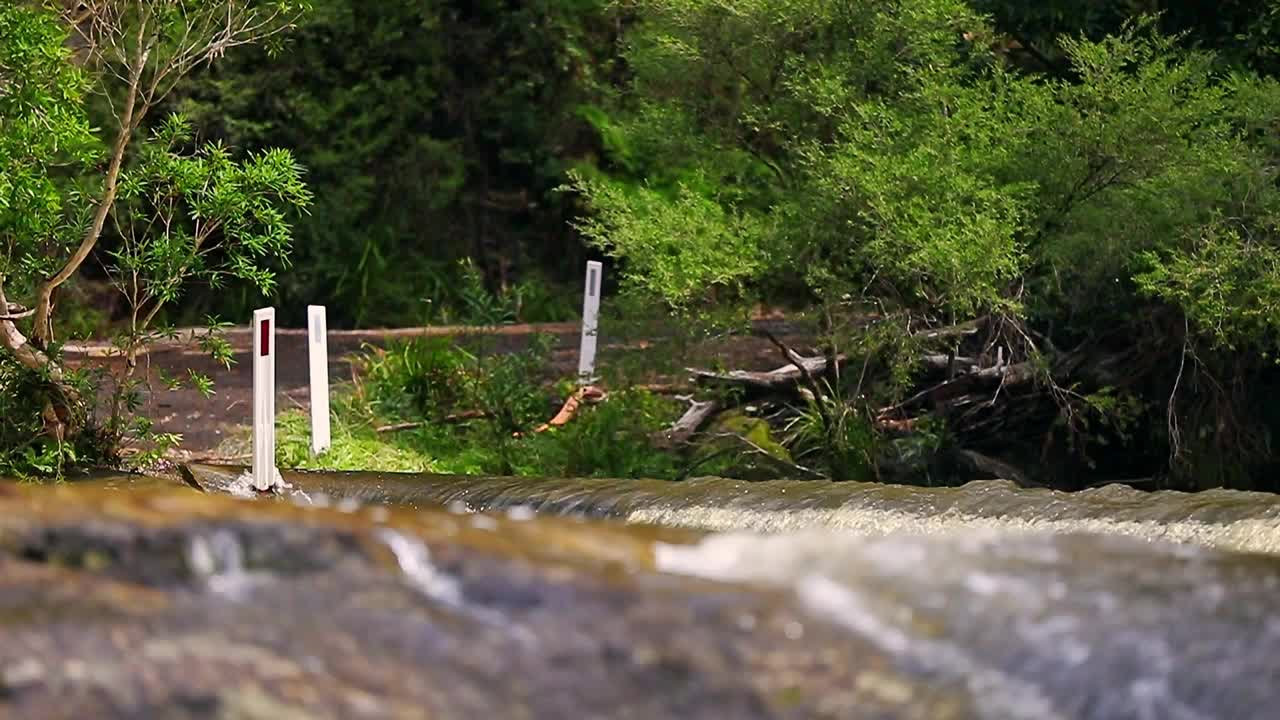 驾驶一辆黑色SUV，在山间湍急的河流和瀑布中穿行视频素材