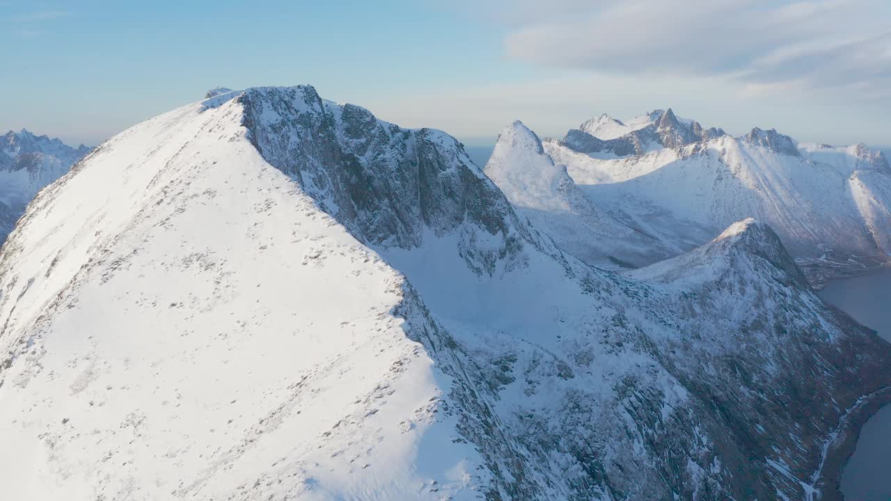 令人惊叹的鸟瞰，挪威海水中覆盖着白雪的高山岩石山峰。令人惊叹的全景峡湾景观Senja在冬季，平静的自然之美。视频素材