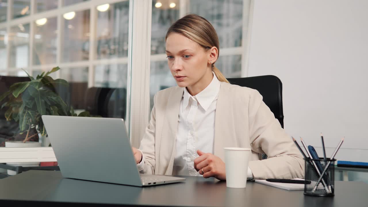 严肃的商业女性在办公室进行在线视频会议。漂亮的工作人员在室内用笔记本电脑进行视频通话。女专业人员在工作场所对着网络摄像头解释项目。视频素材