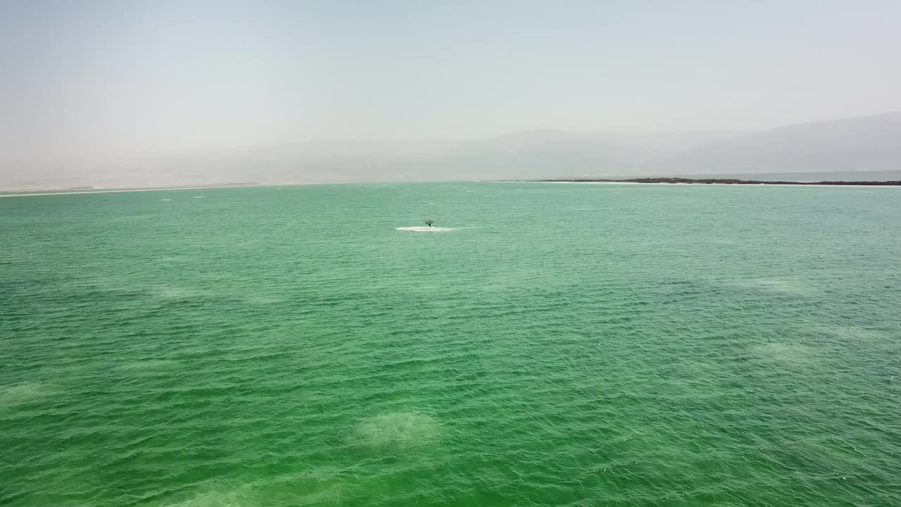 Aerial shot of gazebo on salt lake near hotel against mountains, drone flying forward towards tourists at beach on sunny day – Dead Sea, Israel视频素材