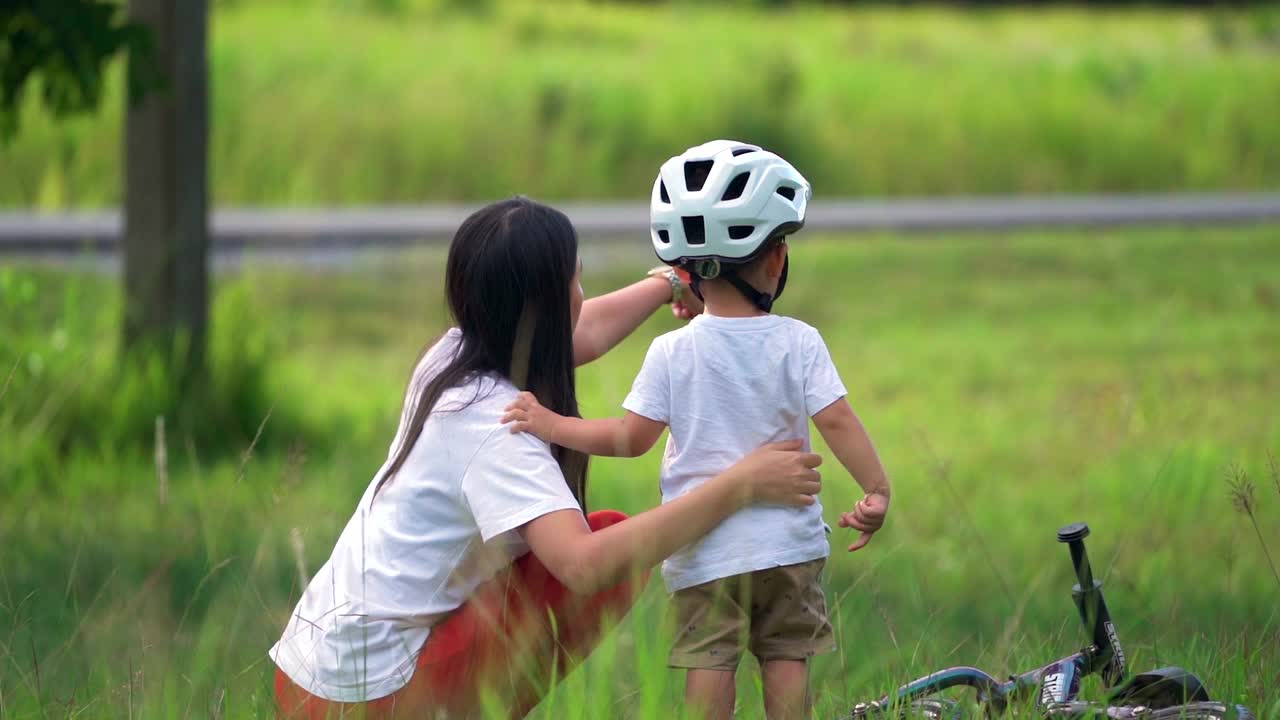 年轻的母亲在自然公园教她的儿子骑自行车。视频素材