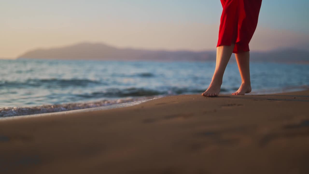 穿红裙子的女人沿着海滩散步。视频素材