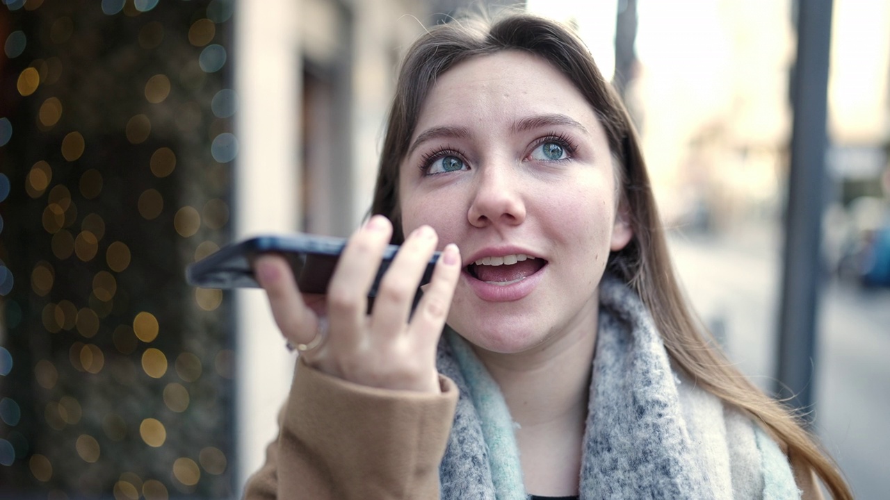 年轻的金发女子微笑自信地在街上通过智能手机发送语音信息视频素材