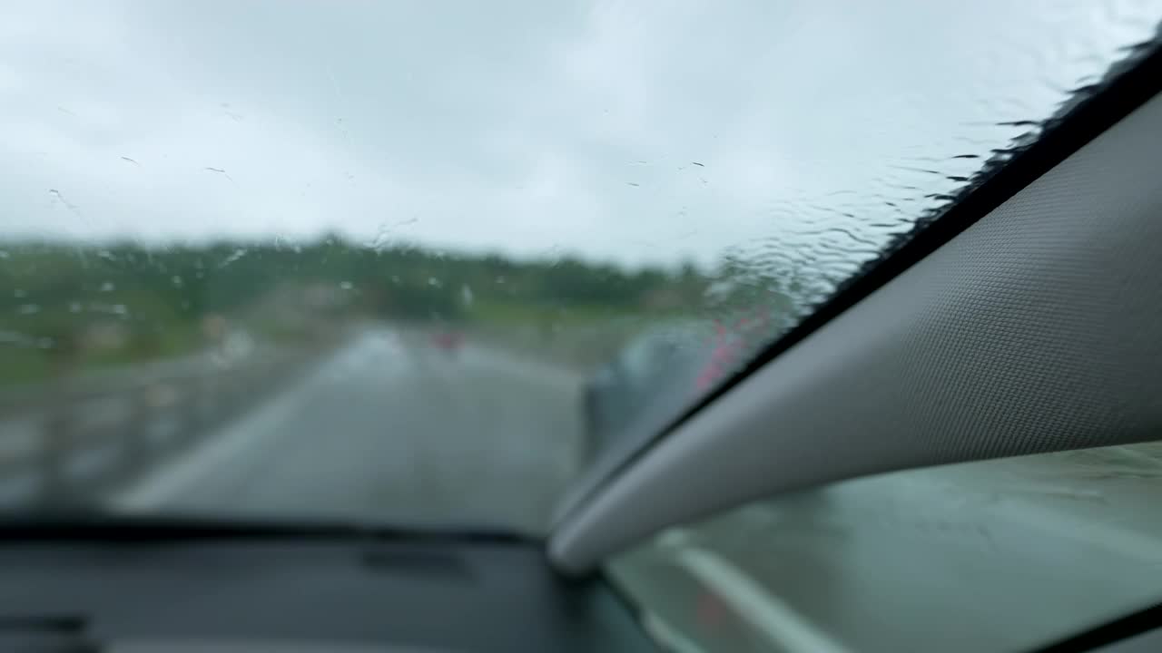 在阴天高速公路恶劣天气下雨时汽车挡风玻璃驾驶特写。车辆在雨中行驶视频素材