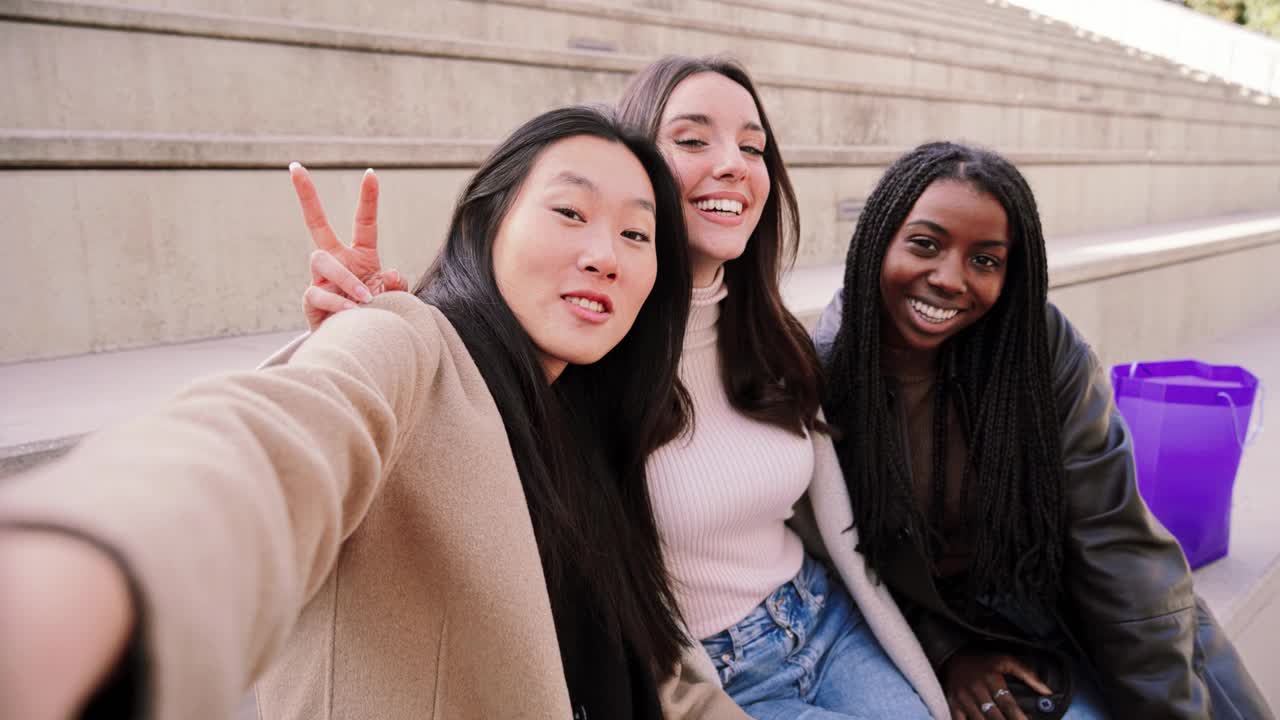 一群快乐的多种族年轻女性对着相机微笑着自拍。三个不同的女孩在户外玩得很开心。最好的朋友在合影。视频素材