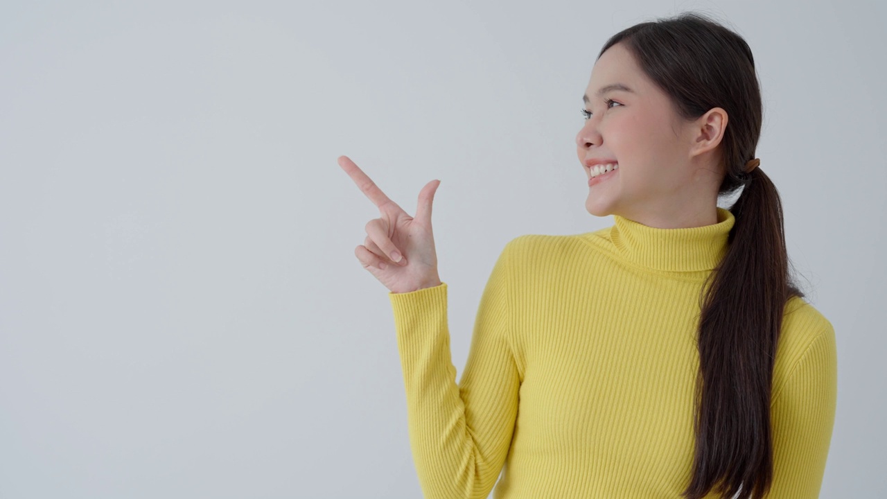 肖像亚洲美丽的女孩指向空白空间孤立的背景。快乐的女人指着什么东西。年轻女性站着，手指向旁边，广告牌，介绍，广告，空间视频素材