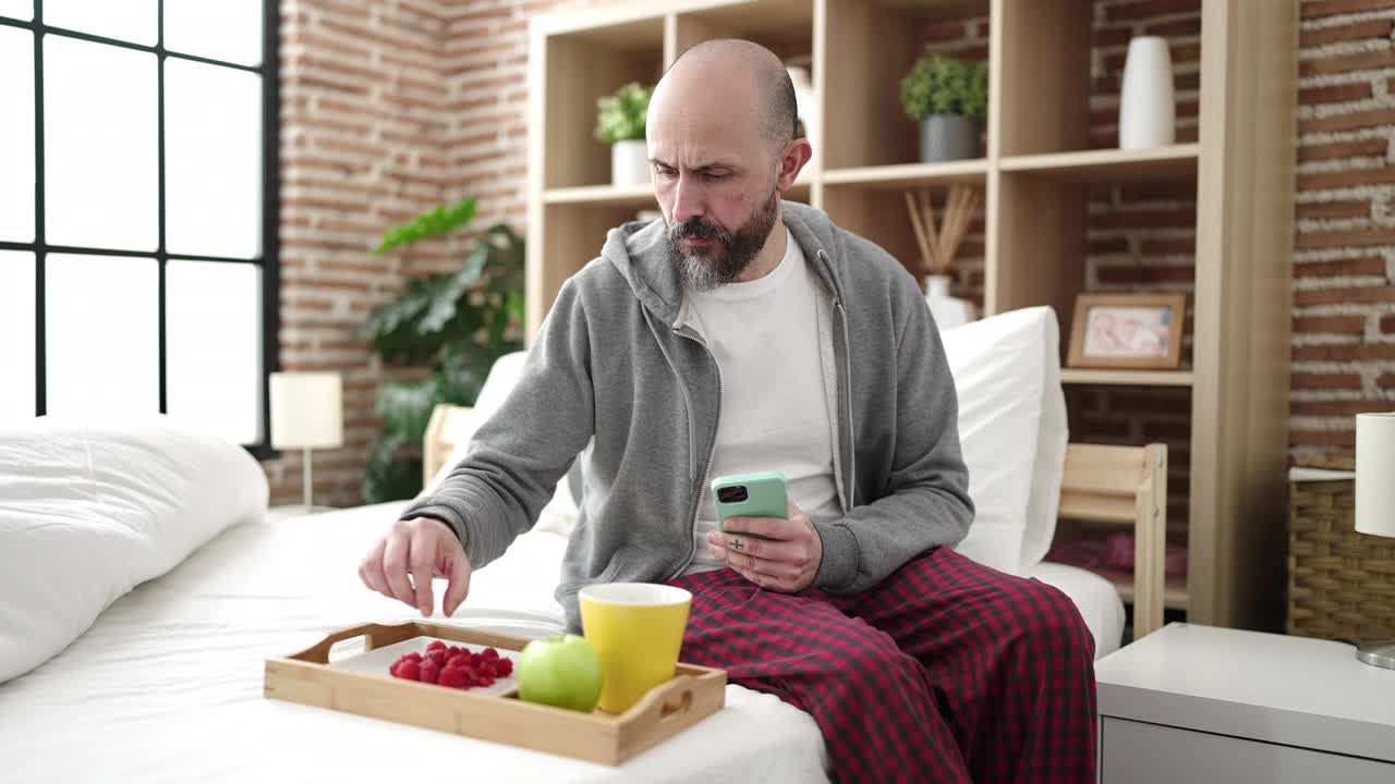 年轻的秃头男子做照片早餐坐在床上在卧室视频素材