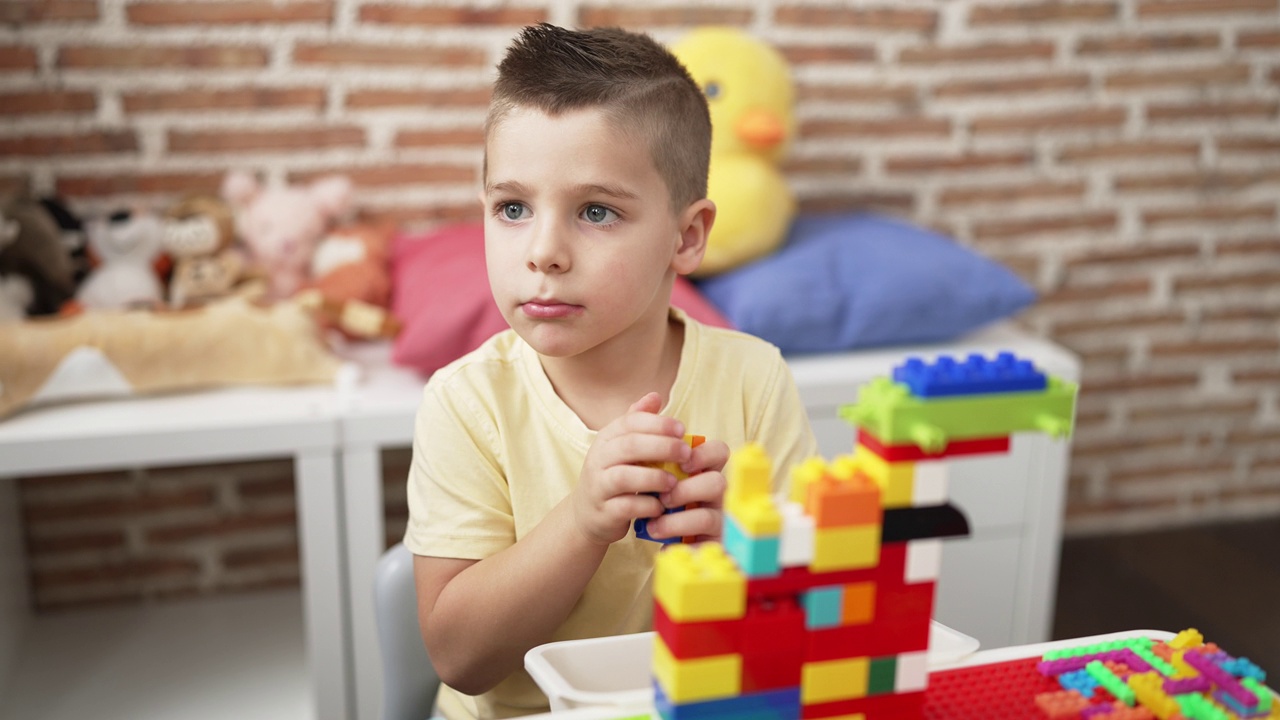 可爱的幼儿坐在幼儿园的桌子上玩积木视频素材