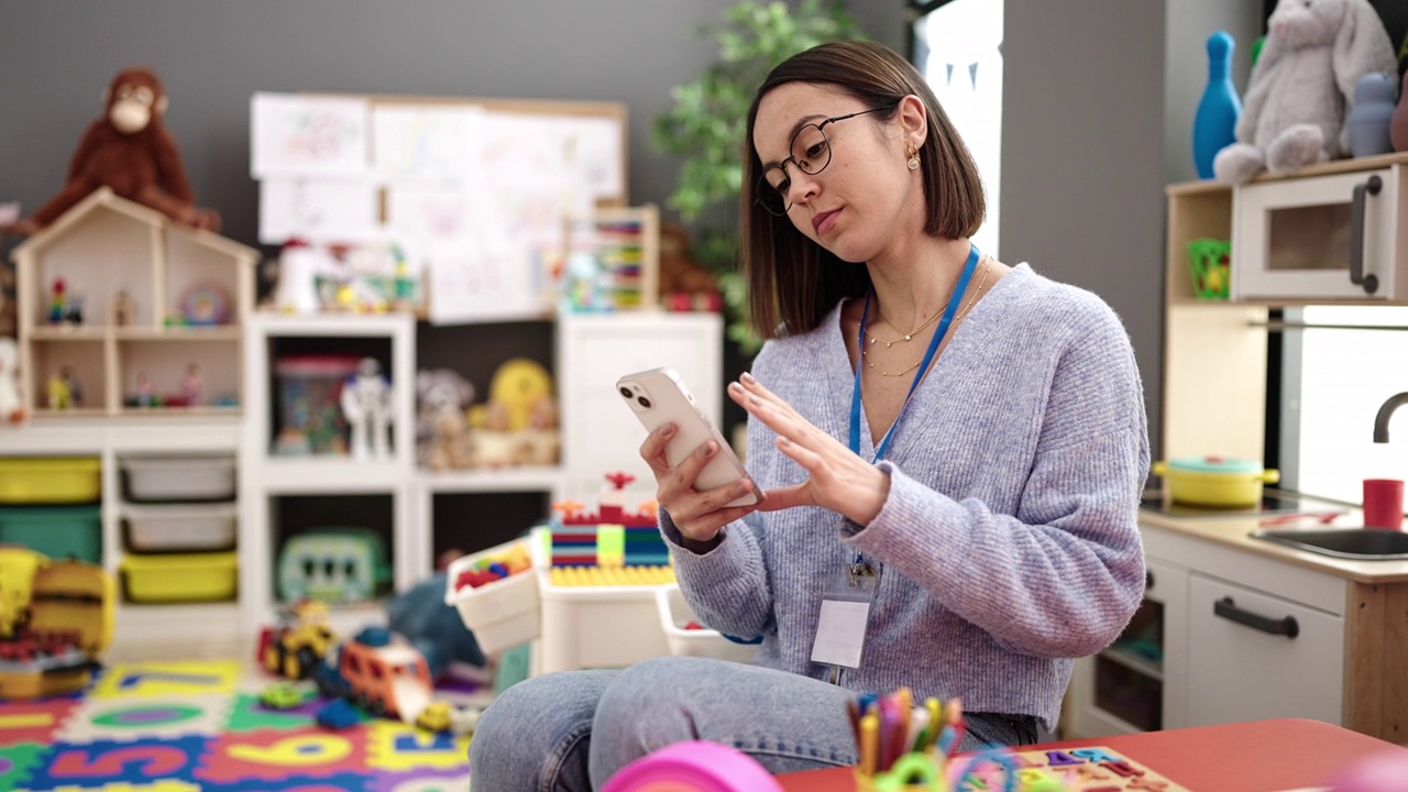 年轻漂亮的西班牙裔女性在幼儿园用智能手机当老师视频素材