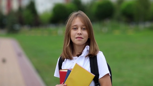 十几岁的女孩拿着书在公园里摆姿势。回到学校。缓慢的莫视频素材