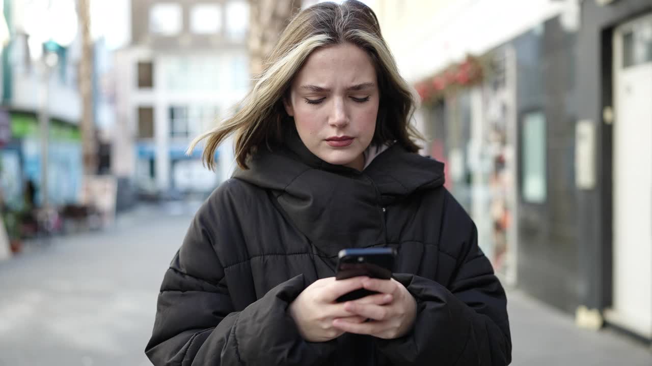 年轻的金发女子在街上使用智能手机，表情严肃视频素材