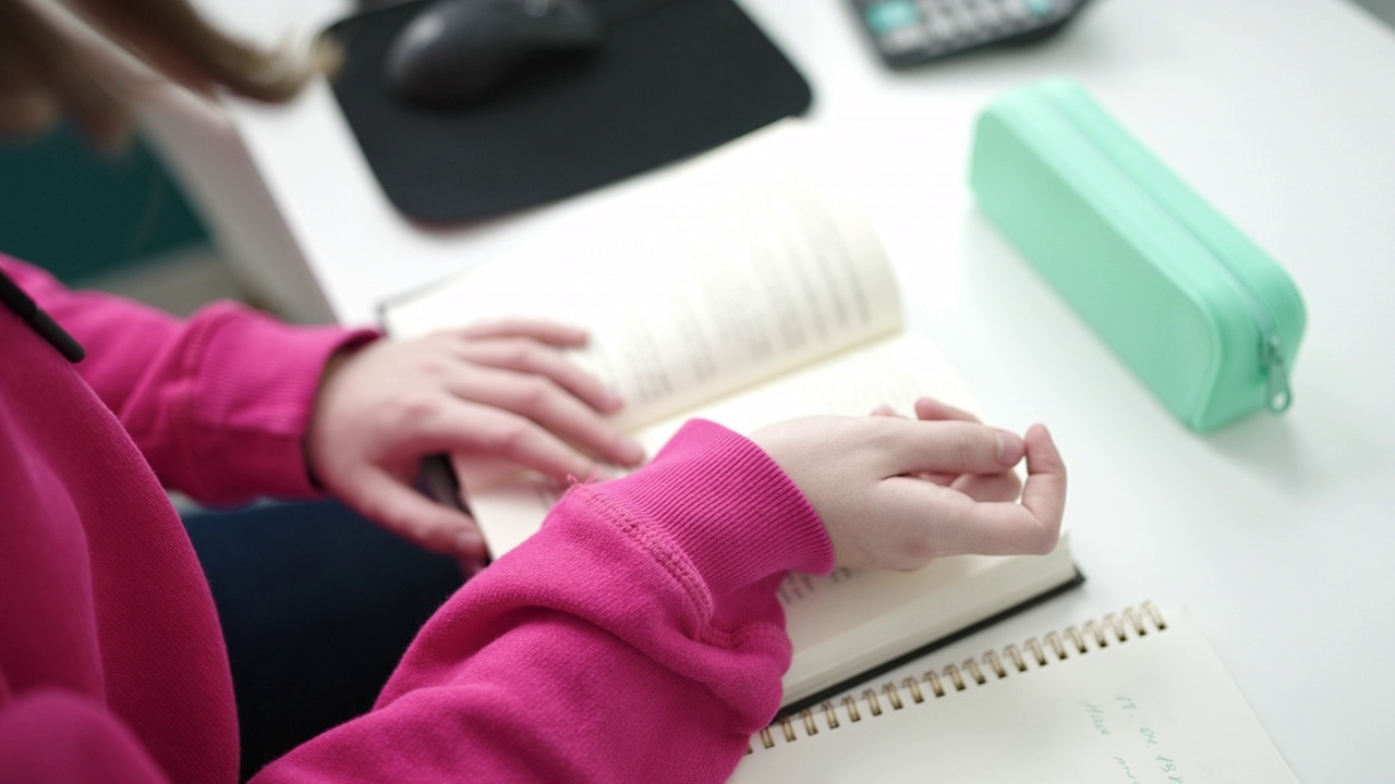 年轻的金发女学生坐在图书馆大学的桌子上看书视频素材