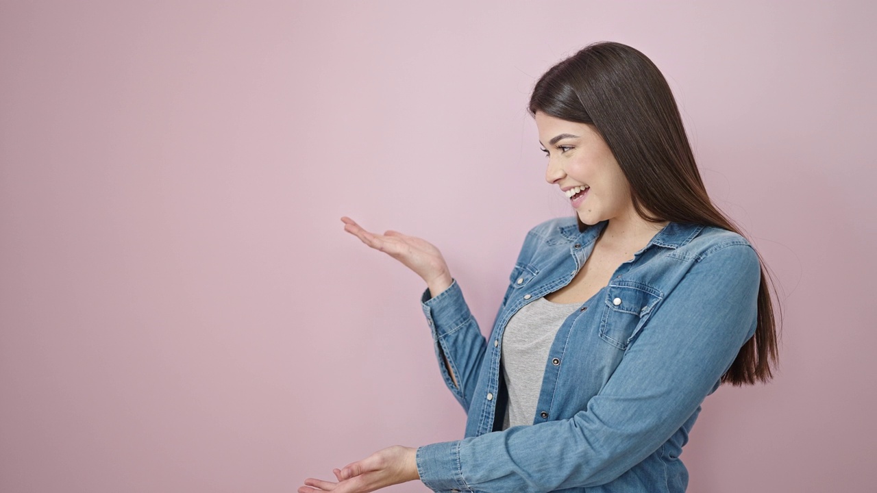 年轻美丽的西班牙女子微笑着自信地用手指指着一侧孤立的粉红色背景视频素材