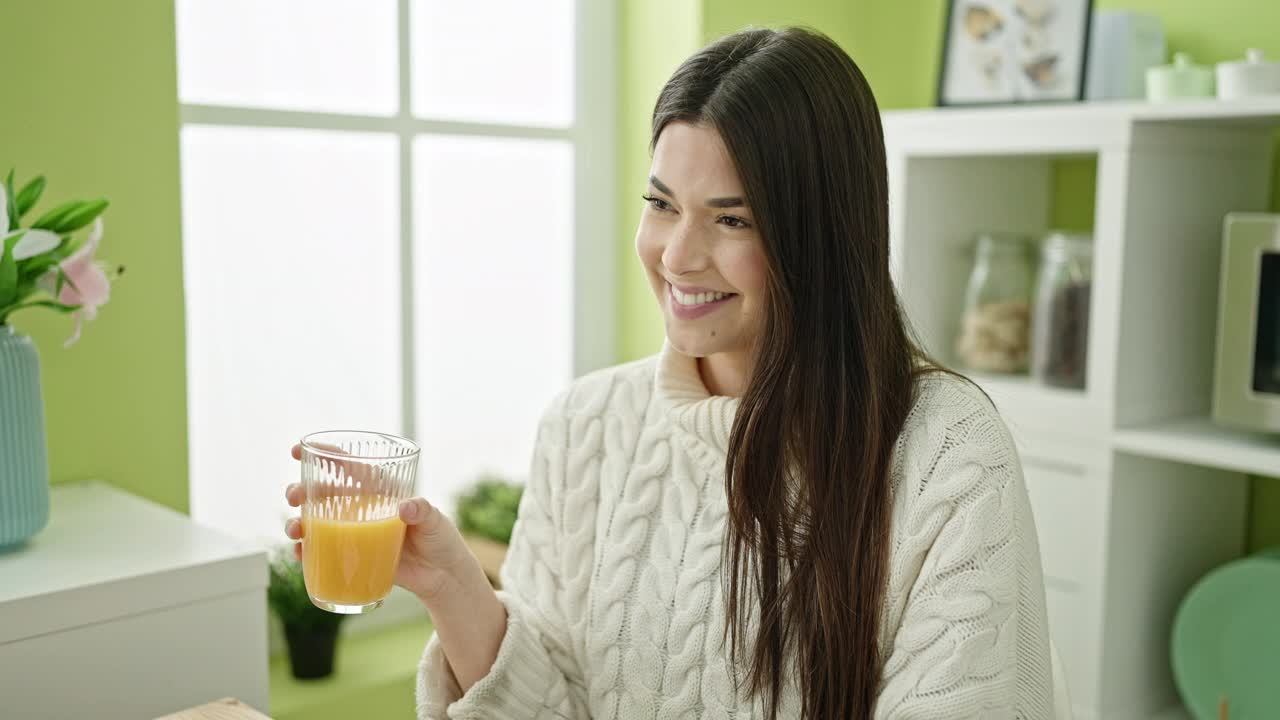 年轻美丽的西班牙女子喝橙汁坐在家里的桌子上视频素材