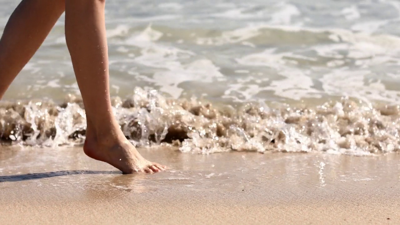 在沙滩上，女性沿着海水波浪行走。漂亮的女人走在海边冲浪。飞溅的水和泡沫。暑假视频素材