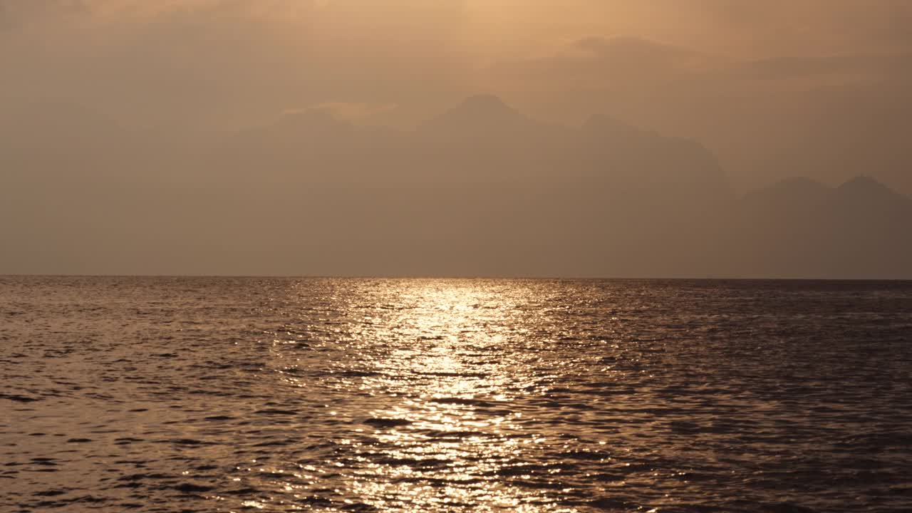 橙色的太阳穿过云层，山脉和海洋。视频素材