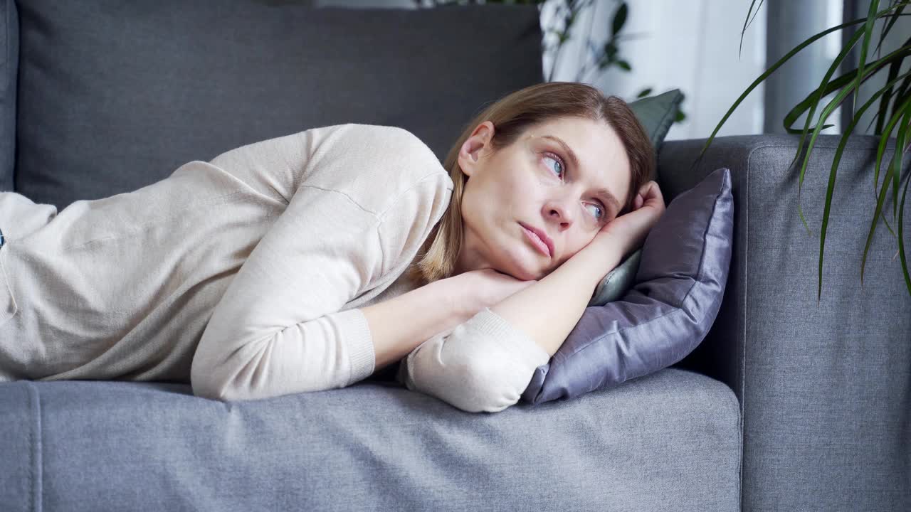 伤心沮丧的孤独女人独自躺在家里的沙发上。冷漠疲倦懒散的女士独自睡在家里的沙发上。视频素材