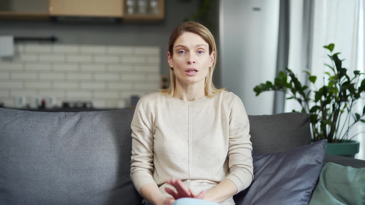 Сonfident woman looking at camera and having video chat conversation while sitting on sofa at home. Webcam view of middle-aged female talking to interlocutor during virtual meeting,视频素材